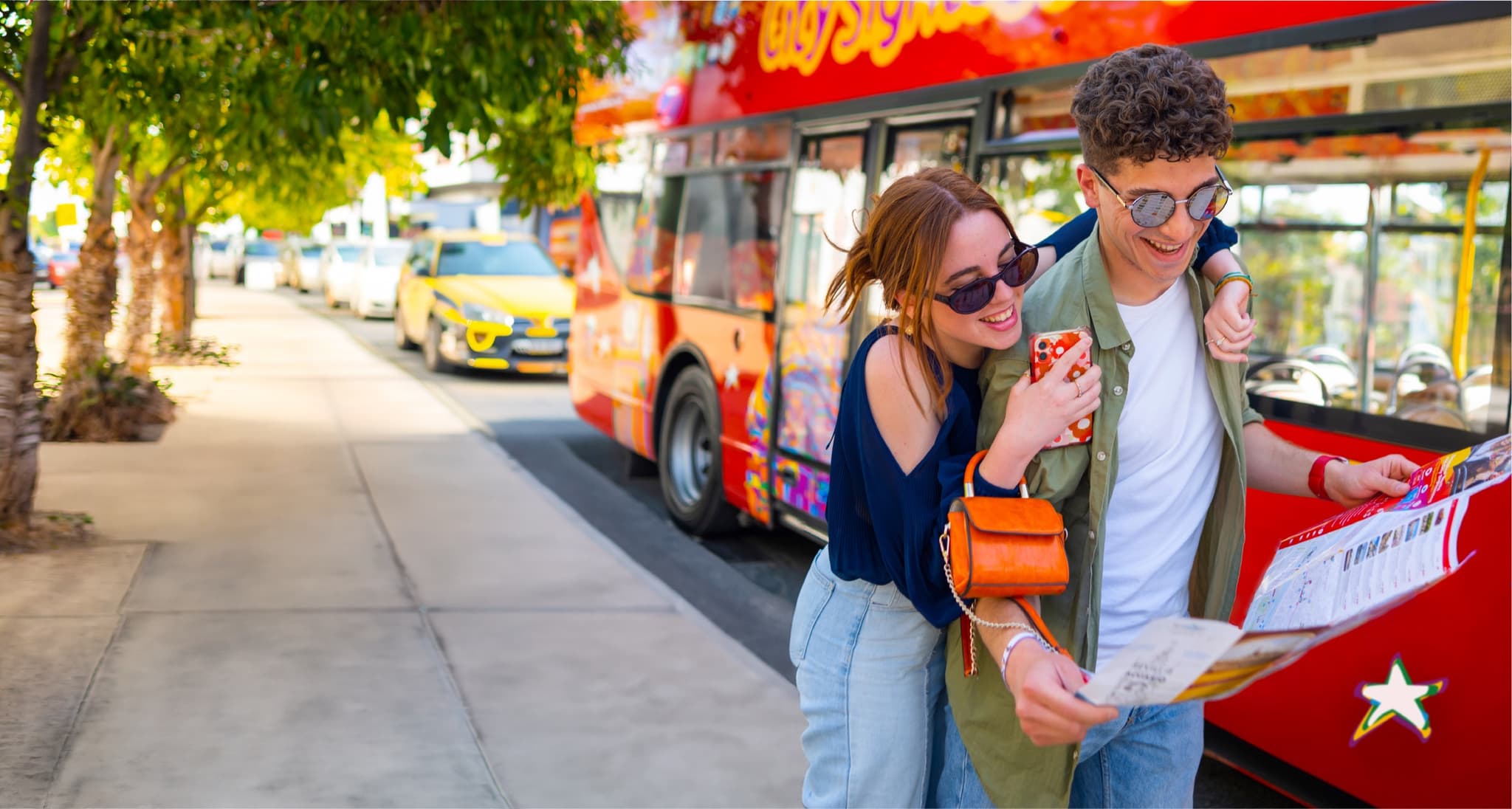 Two friends laughing beside a red City Sightseeing bus